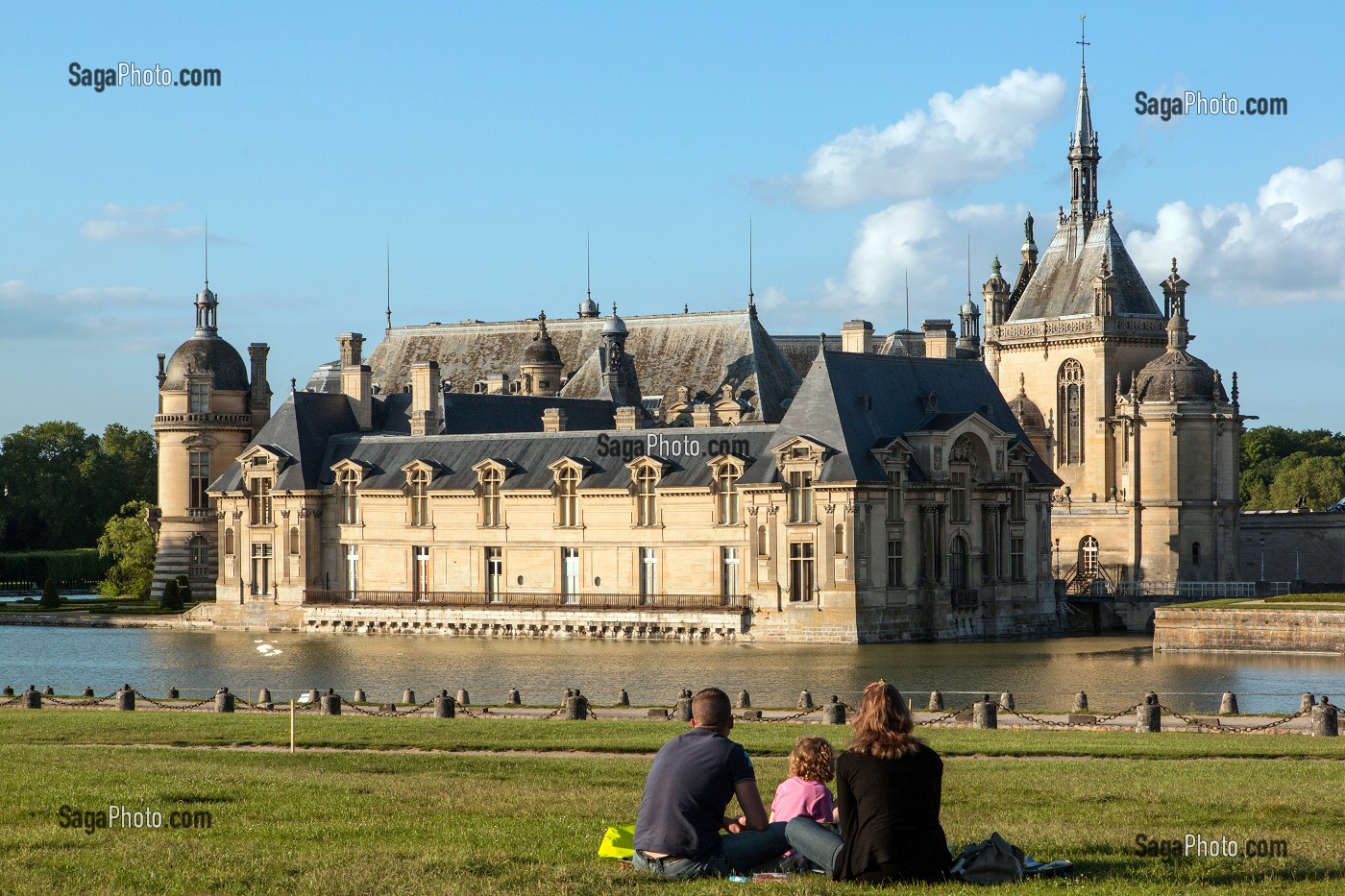 FAMILLE ASSISE SUR LES PELOUSES FACE AU CHATEAU DE CHANTILLY ET A SES DOUVES, OISE (60), FRANCE 