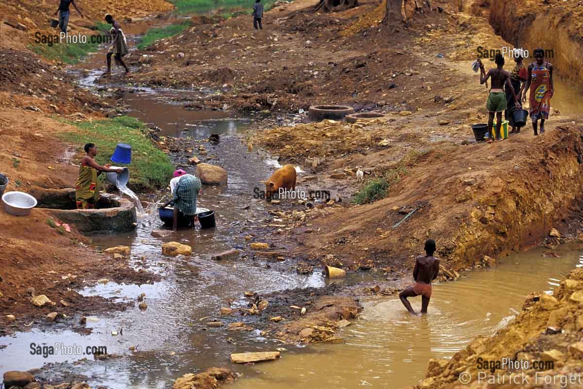 LES FEMMES LAVENT LE LINGE AU PUITS, ENFANTS ET COCHONS SE PARTAGENT L'EAU DU RUISSEAU, AU BURKINA FASO, L'EAU EST RARE ET PRECIEUSE, BOBO-DIOULASSO, BURKINA FASO 