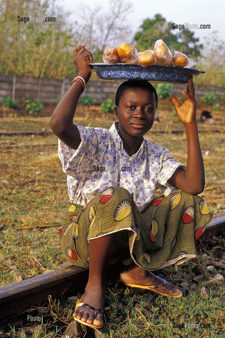 ENFANT VENDANT DE LA NOURRITURE, ASSIS SUR UN RAIL DU CHEMIN DE FER A LA FRONTIERE ENTRE LA COTE D'IVOIRE ET LE BURKINA FASO 