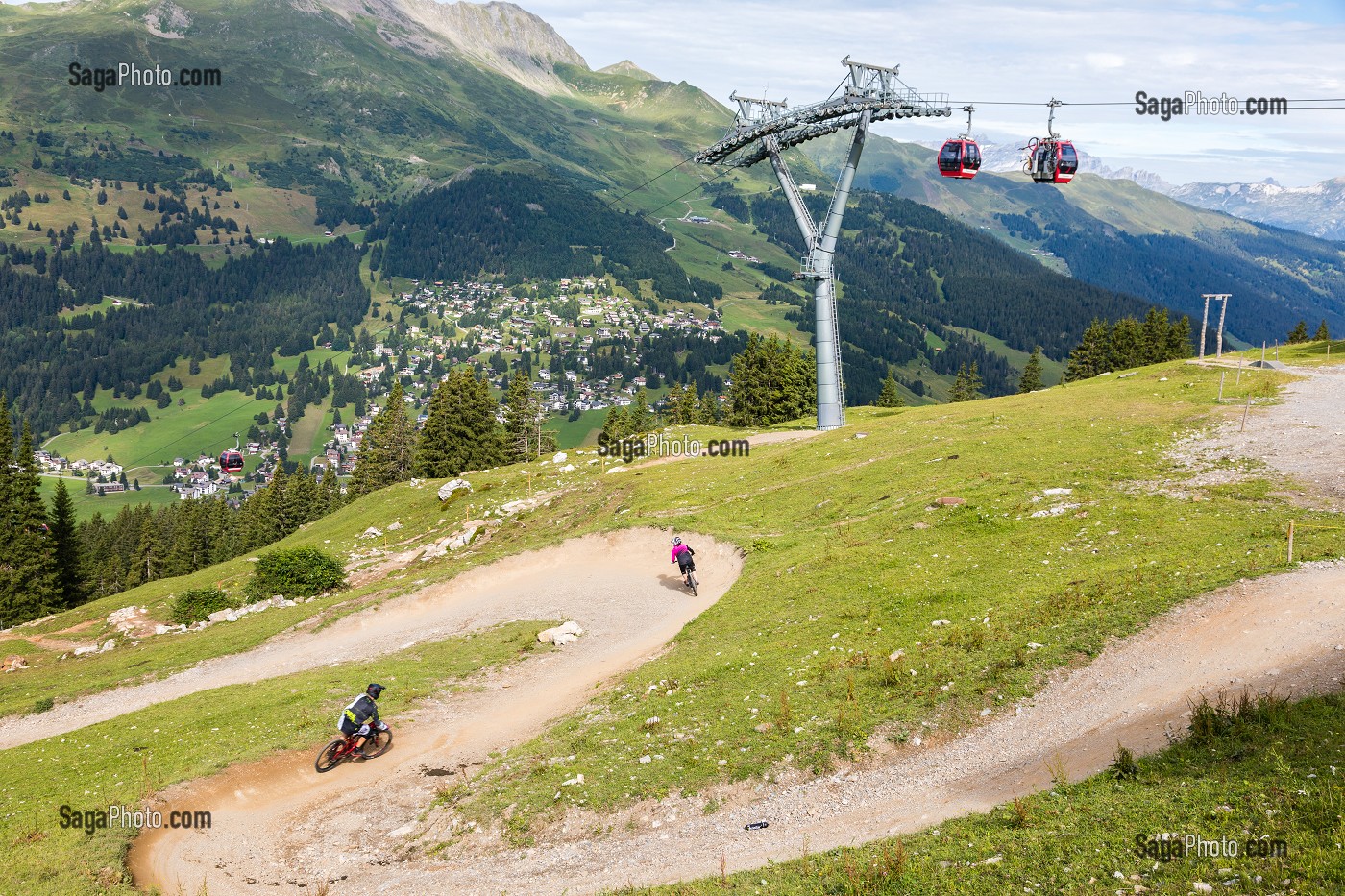 AMATEURS DE VTT DESCENDANT UNE PISTE DE VTT DANS LA STATION DE LENZERHEIDE AVEC LES TELECABINES ET LES ALPES SUISSES EN FOND, LENZERHEIDE, CANTON DES GRISONS, SUISSE 