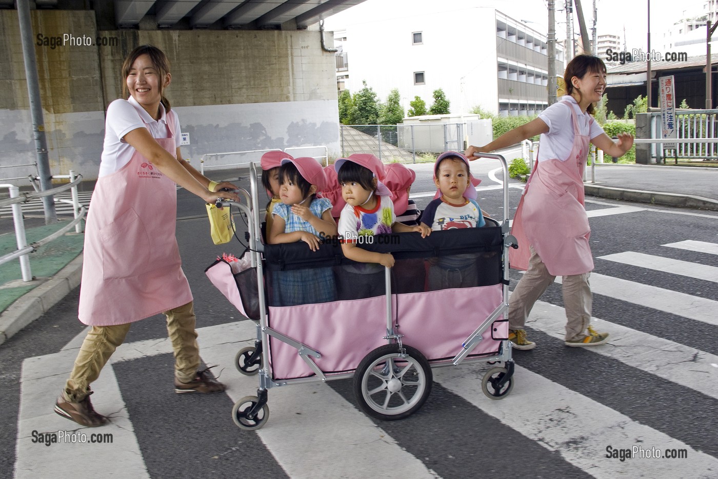 ENFANTS DANS UNE POUSSETTE COLLECTIVE TIREE PAR DES PUERICULTRICES JAPONAISES SUR UN PASSAGE PIETON, TOKYO, JAPON 