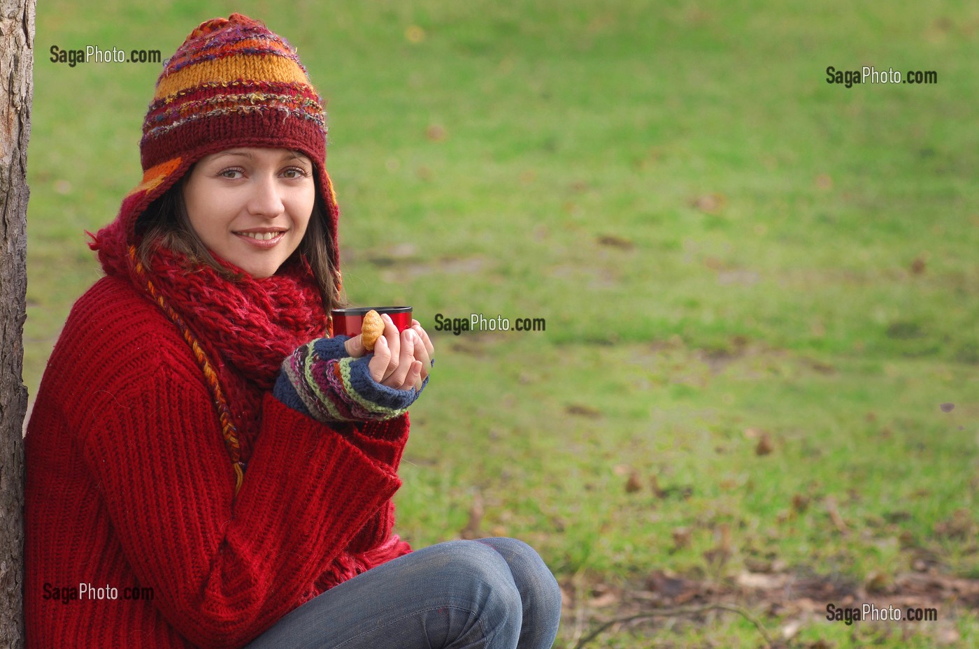FROID ET CALORIES. JEUNE FEMME SE RECHAUFFANT ET SE RESTAURANT AVEC UNE BOISSON CHAUDE ET UN PETIT GATEAU, LORS D'UNE PROMENADE DANS LA NATURE 
