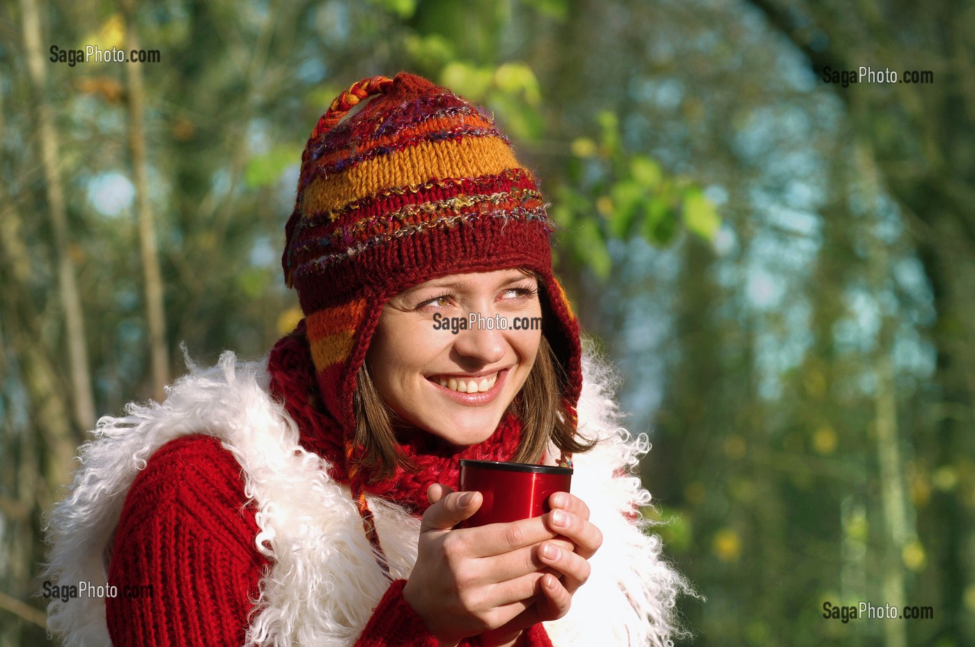 JEUNE FEMME SE RECHAUFFANT AVEC UNE BOISSON CHAUDE, LORS D'UNE PROMENADE EN FORET 