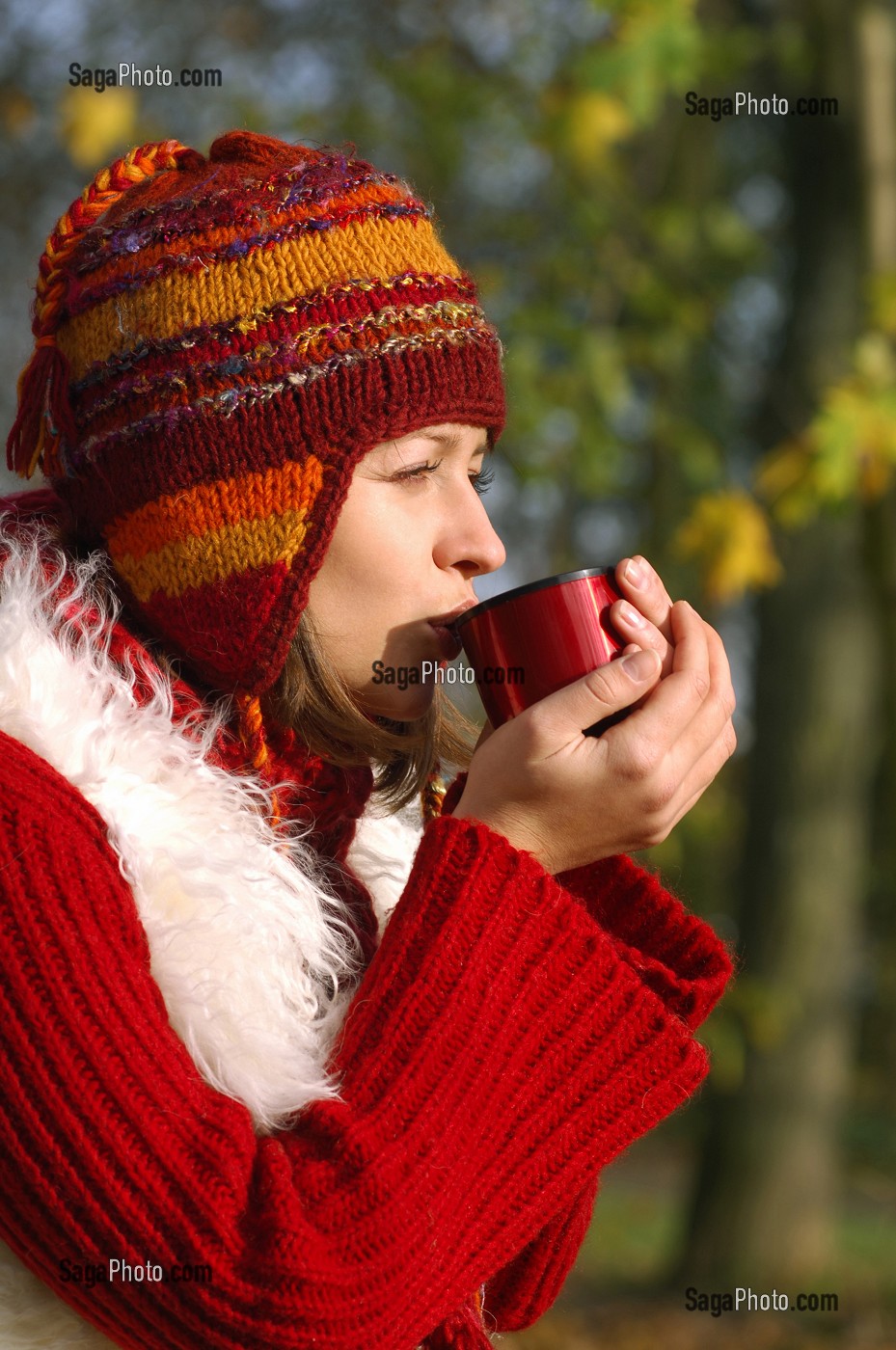 JEUNE FEMME SE RECHAUFFANT AVEC UNE BOISSON CHAUDE, LORS D'UNE PROMENADE EN FORET 