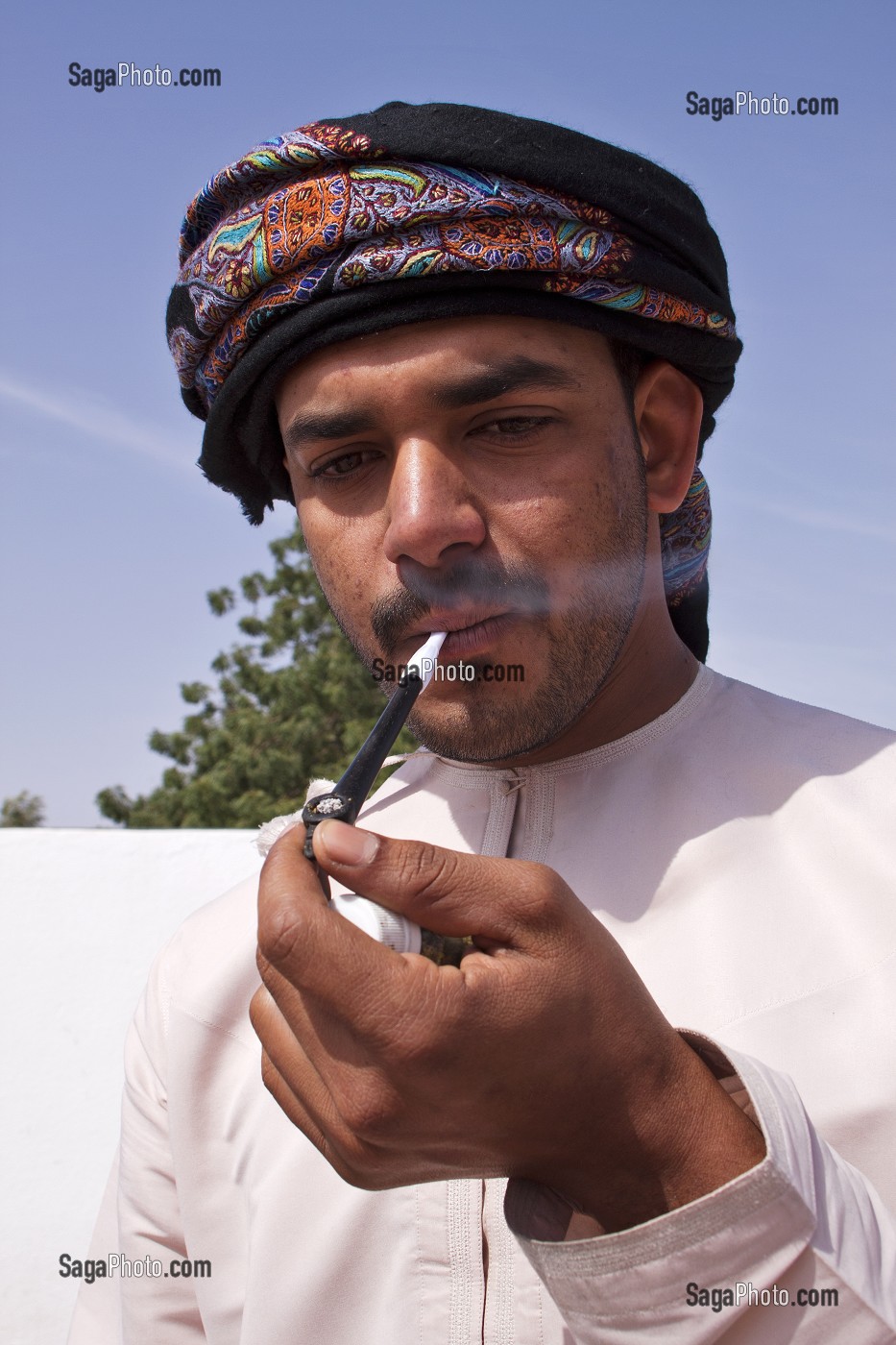 HOMME EN HABIT TRADITIONNEL (DISHDASHA) FUMANT LA PIPE OMANAISE, ROUTE DE WAHIBA SANDS, SULTANAT D'OMAN, MOYEN-ORIENT 