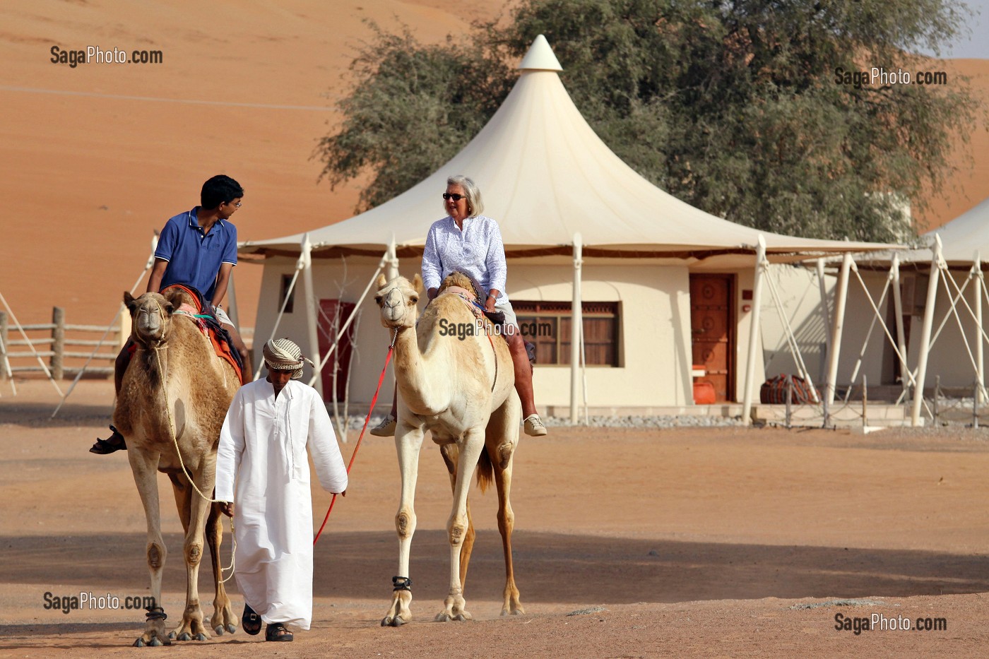 TOURISTE INDIEN ET TOURISTE BRITANNIQUE FAISANT UN TOUR A DOS DE DROMADAIRES DANS L'ENCEINTE DU COMPLEXE TOURISTIQUE DESERT NIGHT CAMP, DESERT DE WAHIBA SANDS, SULTANAT D'OMAN, MOYEN-ORIENT 