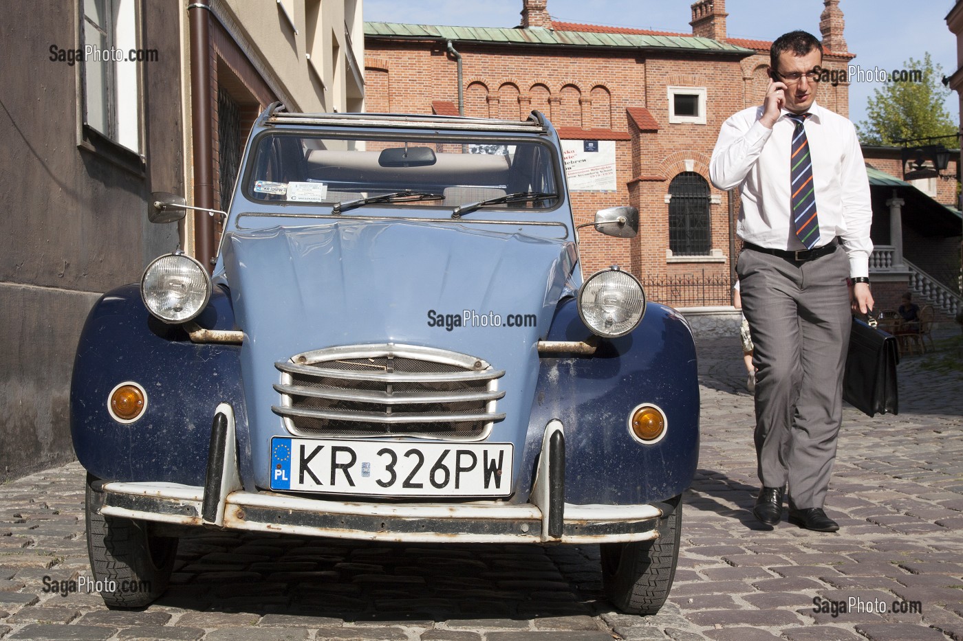 CONTRASTE ENTRE UNE VIEILLE 2CV CITROEN ET UN HOMME D'AFFAIRES AU TELEPHONE DANS UNE RUE DU QUARTIER JUIF DE KAZIMIERZ, CRACOVIE, POLOGNE 