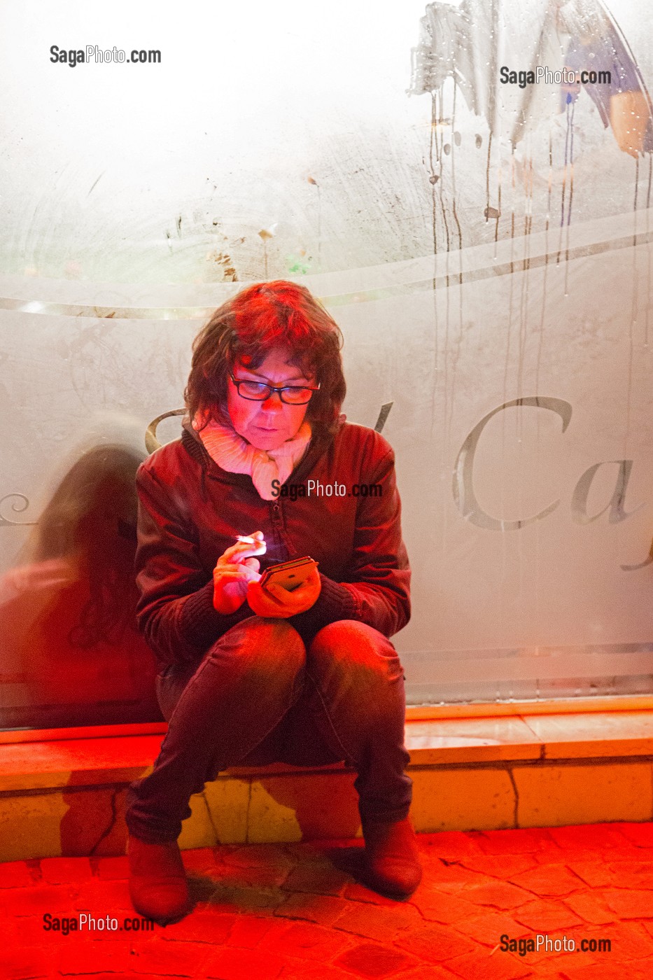 FEMME AVEC UN TELEPHONE PORTABLE EN TRAIN DE FUMER UNE CIGARETTE EN DEHORS DU CAFE EN HIVER, FRANCE 