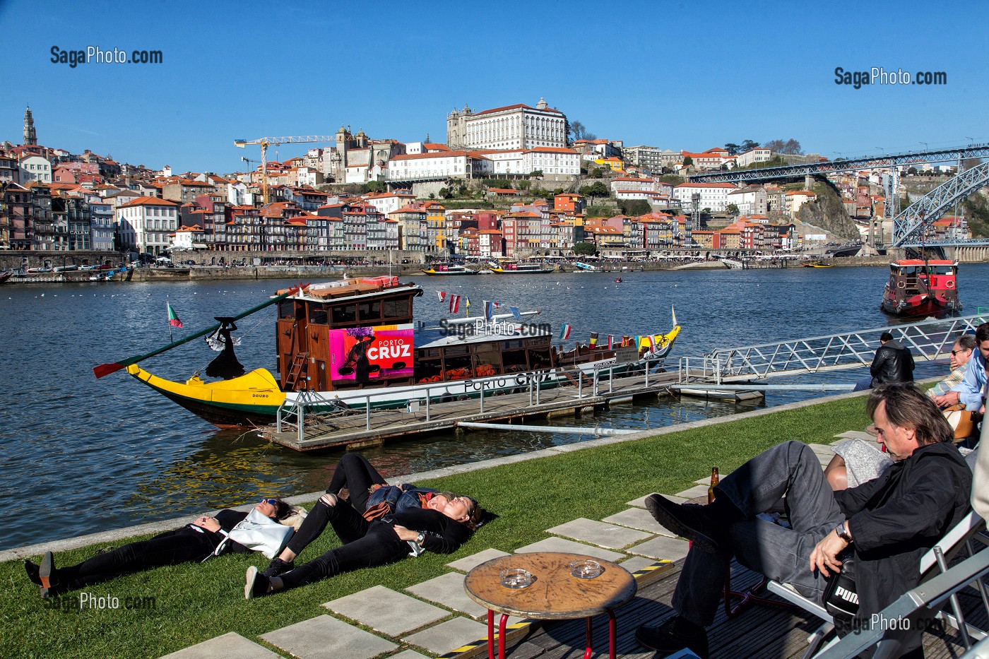 PETITE SIESTE APRES LA DEGUSTATION, PROMENEURS AU BORD DU DOURO DEVANT LES BATEAUX A FOND PLAT POUR LE TRANSPORT DU VIN (BARCOS RABELOS) AVEC LA VILLE ET LE PALAIS EPISCOPAL VILA NOVA DE GAIA, PORTO, PORTUGAL 