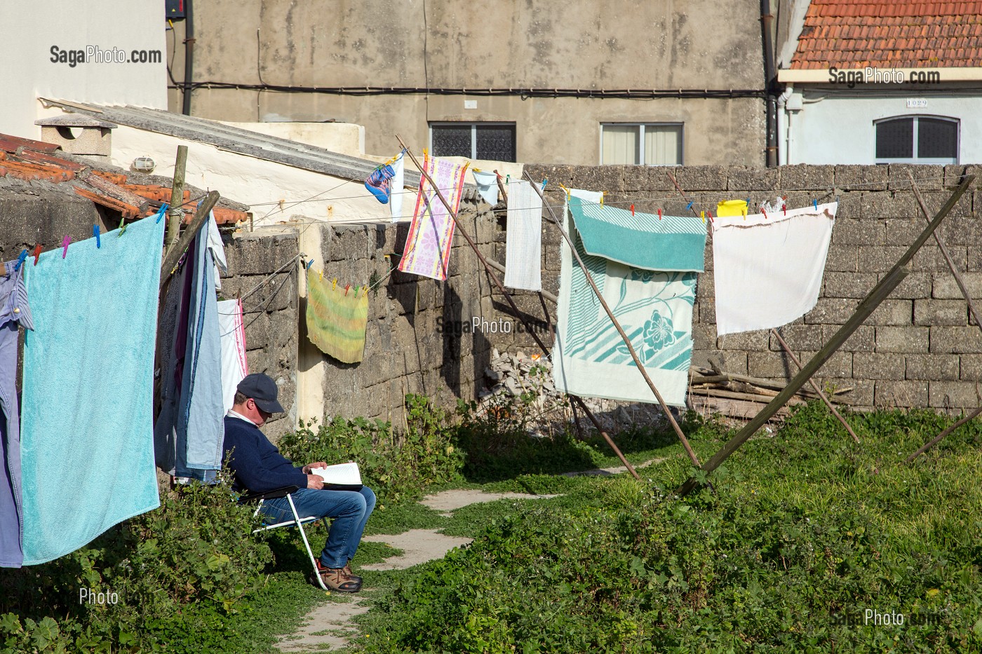 HOMME ASSIS DANS SON JARDIN EN TRAIN DE LIRE AU MILIEU DU LINGE A SECHER, VILLE BALNEAIRE D'ESPINHO, PORTUGAL 