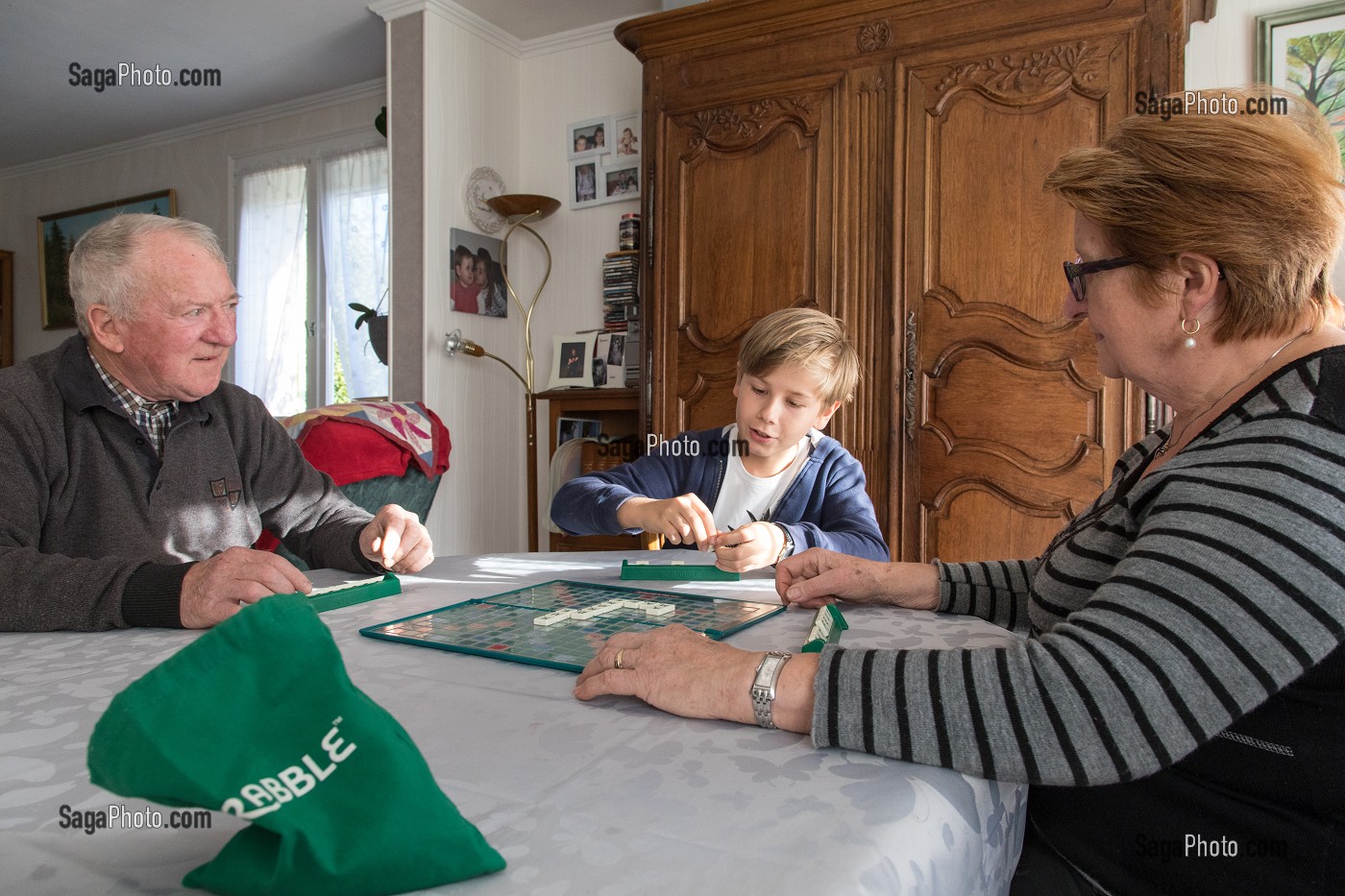 COUPLE DE PERSONNES AGEES AVEC LEUR PETIT-FILS EN TRAIN DE JOUER AU SCRABBLE DANS LA MAISON, VILLE DE VERNEUIL-SUR-AVRE (27), FRANCE 