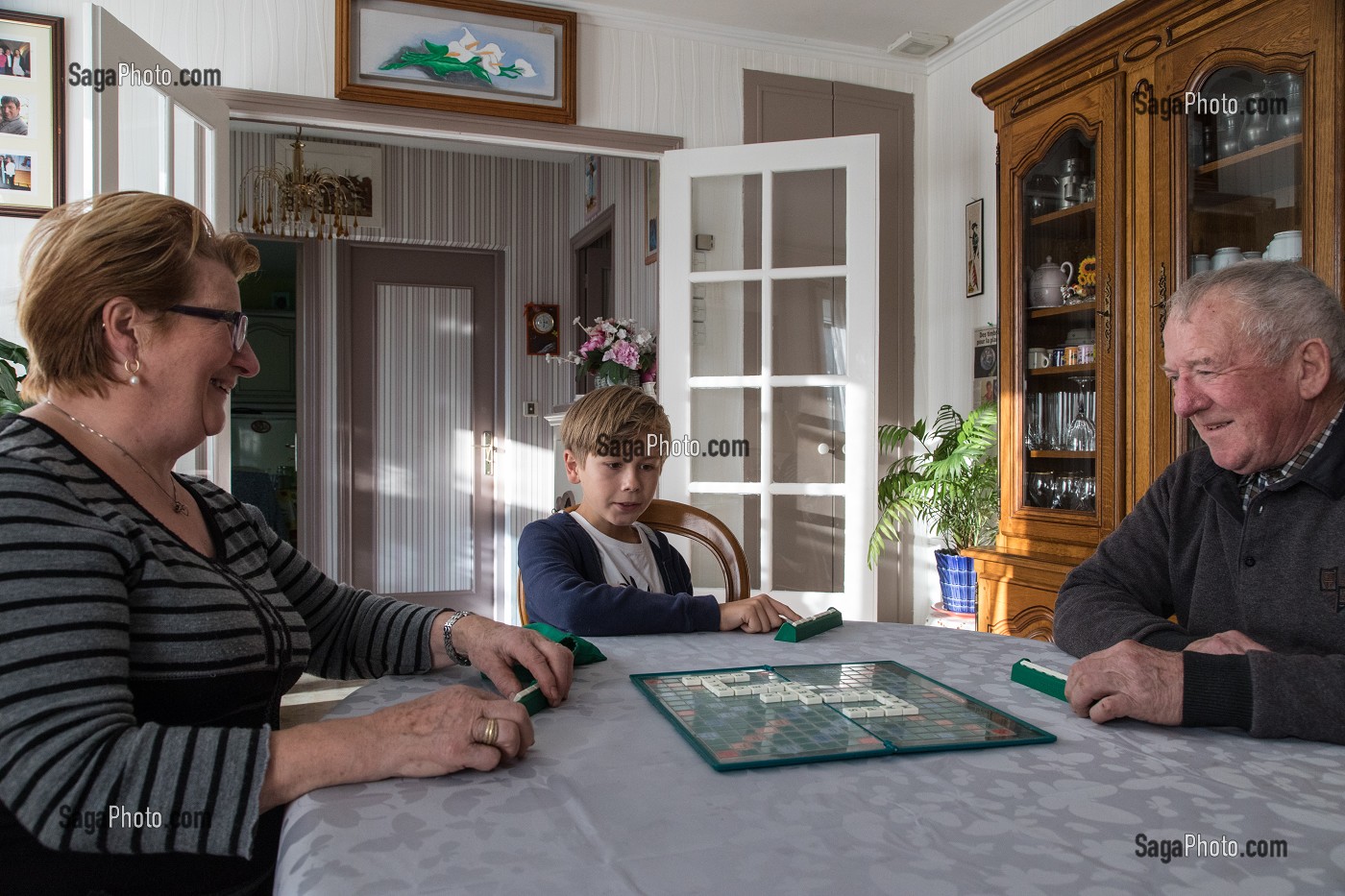 COUPLE DE PERSONNES AGEES AVEC LEUR PETIT-FILS EN TRAIN DE JOUER AU SCRABBLE DANS LA MAISON, VILLE DE VERNEUIL-SUR-AVRE (27), FRANCE 