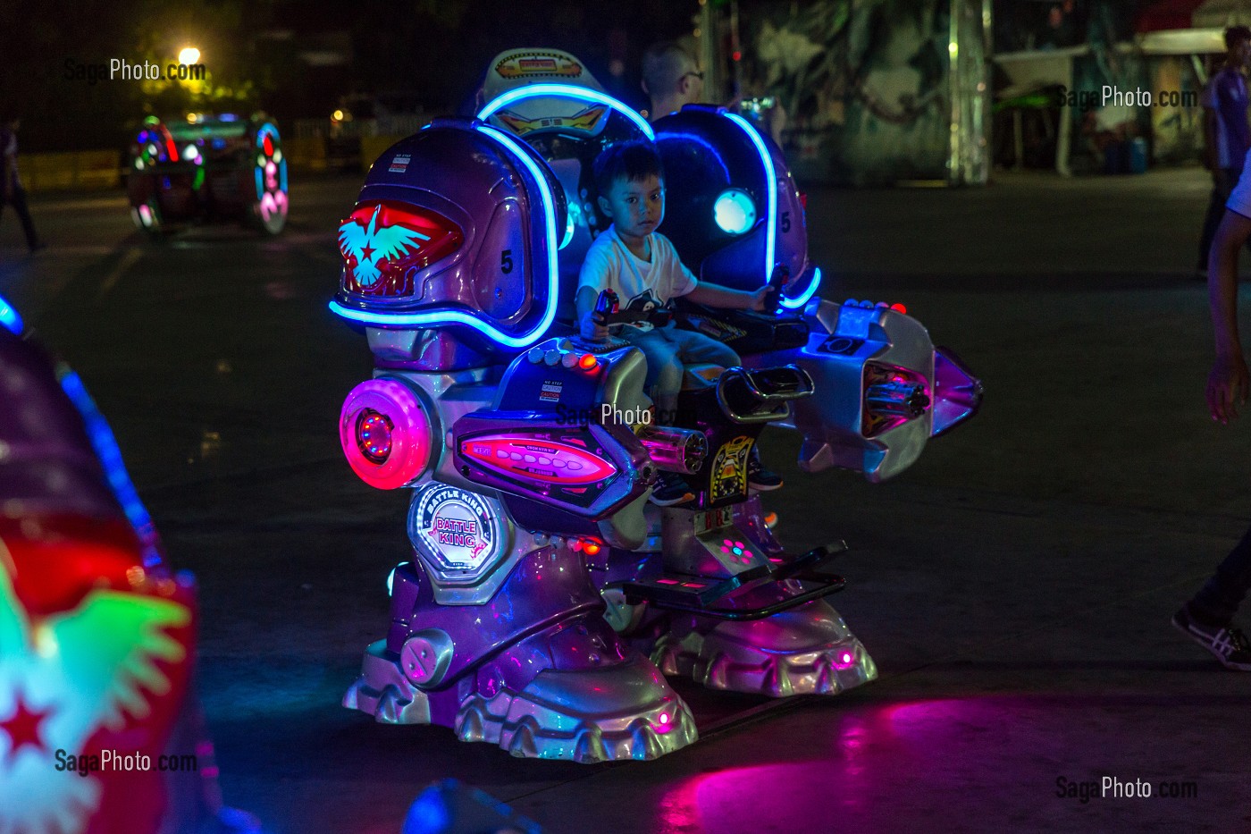 PETIT GARCON JOUANT DANS LA RUE AVEC UN MANEGE DE ROBOT, SCENE DE RUE, SCENE DE NUIT, VILLE DE BANGKOK, THAILANDE 