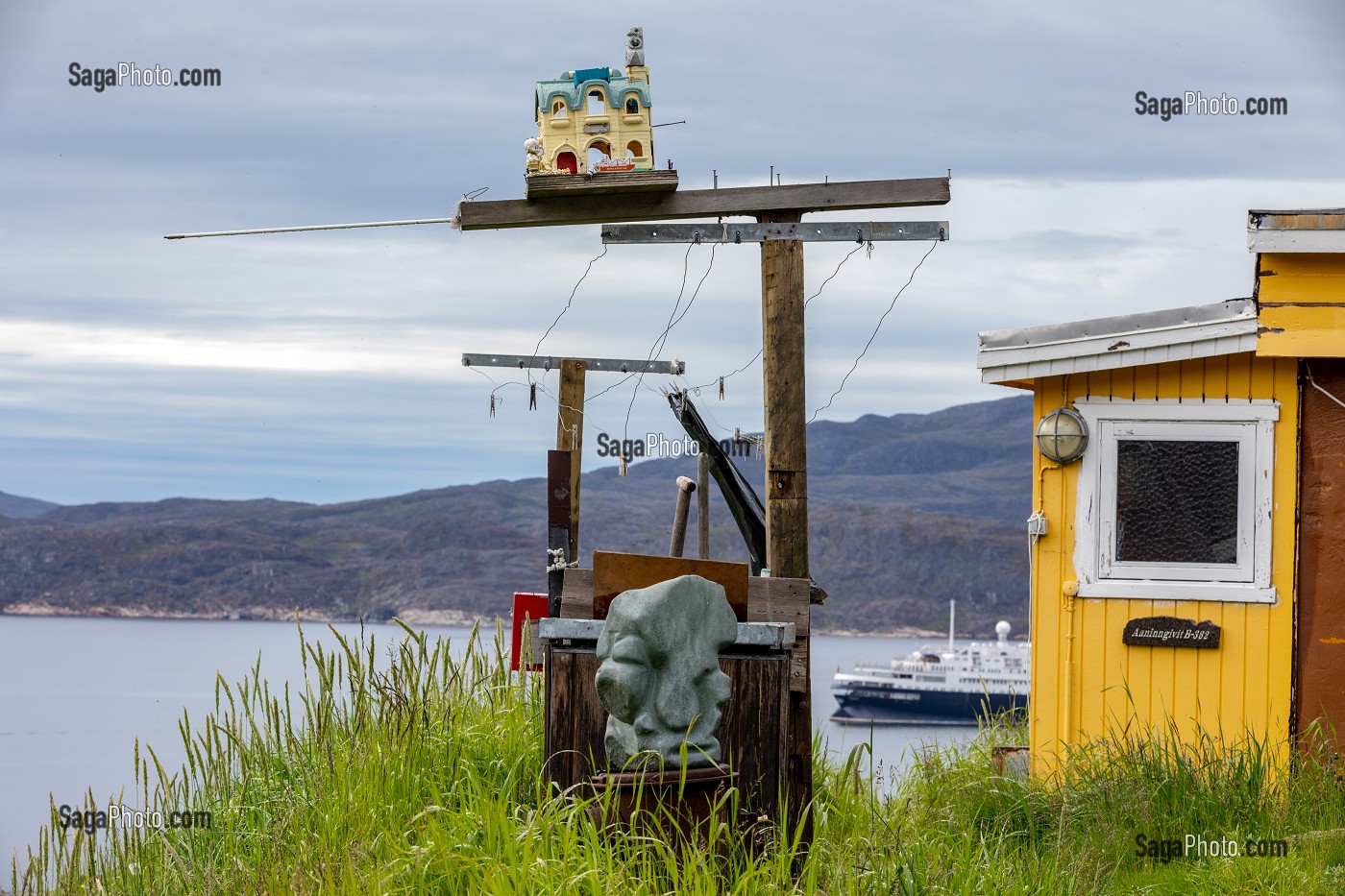 SCULPTURE DE PIERRE DEVANT FIL A LINGE, MAISON TRADITIONNELLE COLOREE JAUNE, VILLE DE QAQORTOQ, GROENLAND, DANEMARK 