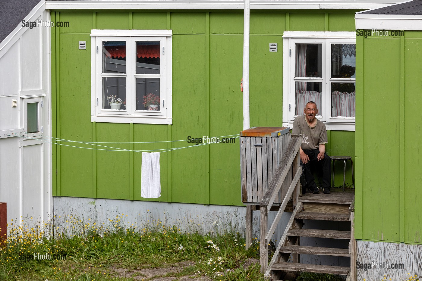 HABITANT FUMANT UNE CIGARETTE DEVANT SA MAISON TRADITIONNELLE EN BOIS DE COULEUR VERTE, VILLE DE QAQORTOQ, GROENLAND, DANEMARK 