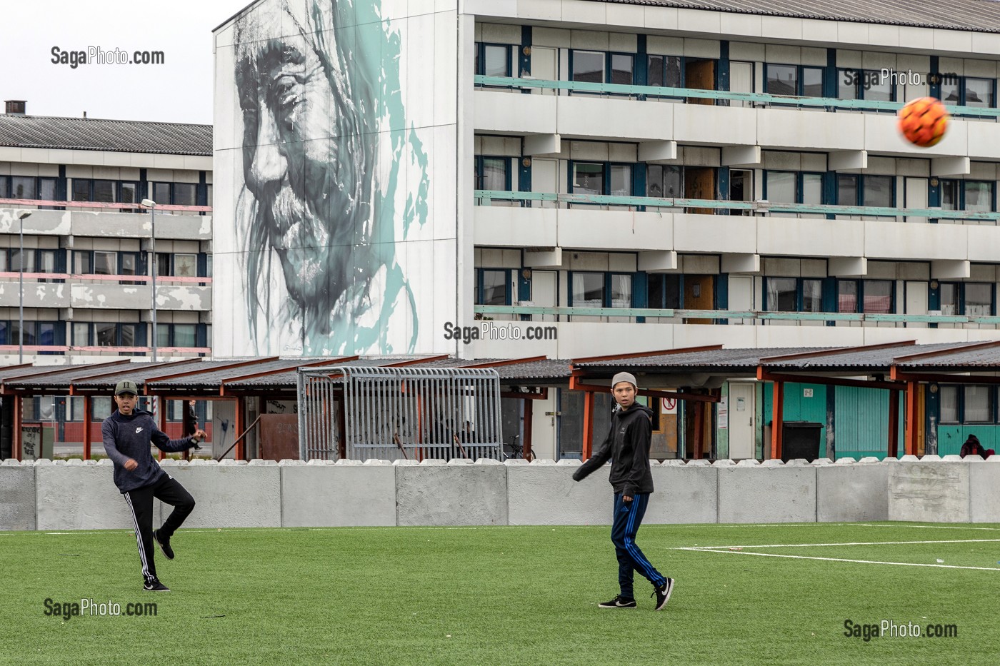 JEUNES JOUANT AU FOOTBALL DEVANT UNE CITE HLM PEINTE AVEC LE PORTRAIT D'UN INUIT, NUUK, GROENLAND, DANEMARK 