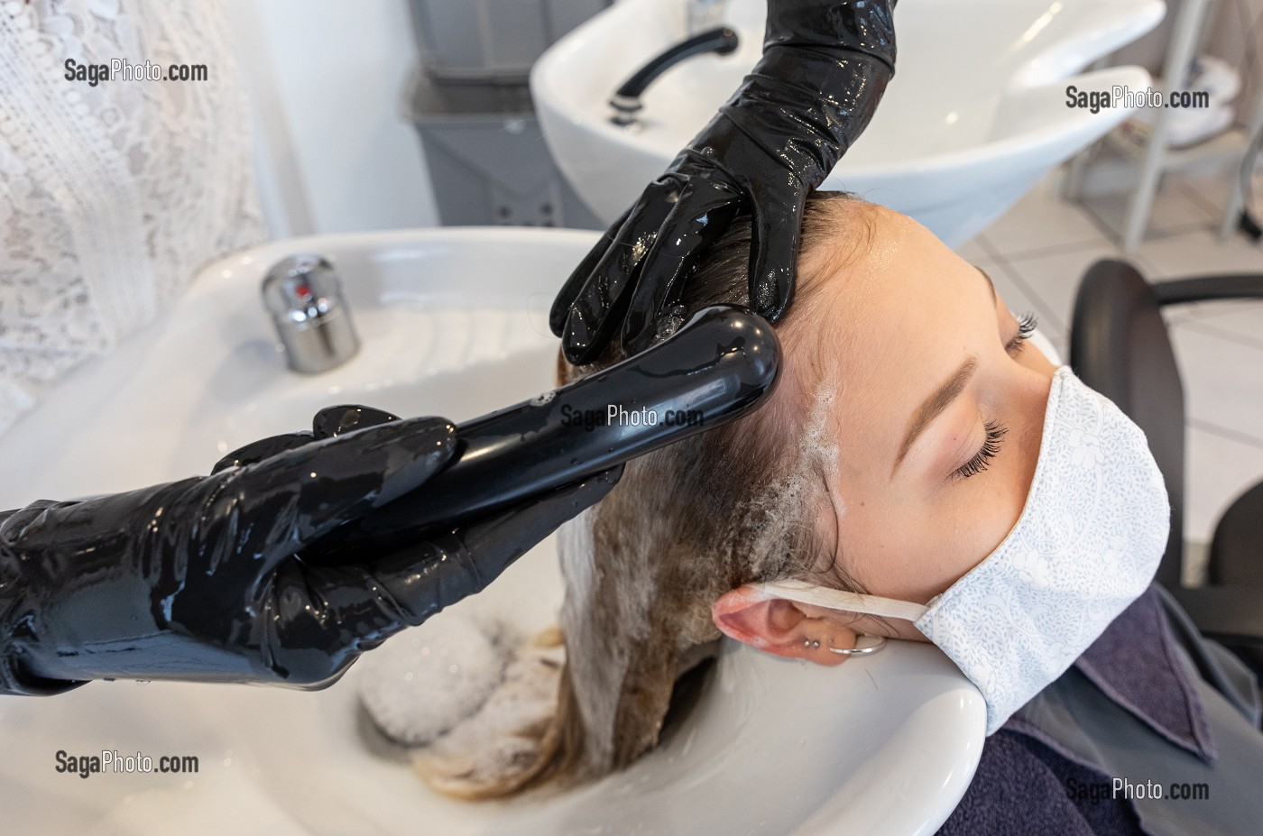 LAVAGE DES CHEVEUX, COIFFEUSE AVEC SON MASQUE DE PROTECTION ET SES GANTS EN TRAIN DE COIFFER UNE CLIENTE DANS UN SALON DE COIFFURE VIDE, RUGLES, NORMANDIE, FRANCE 