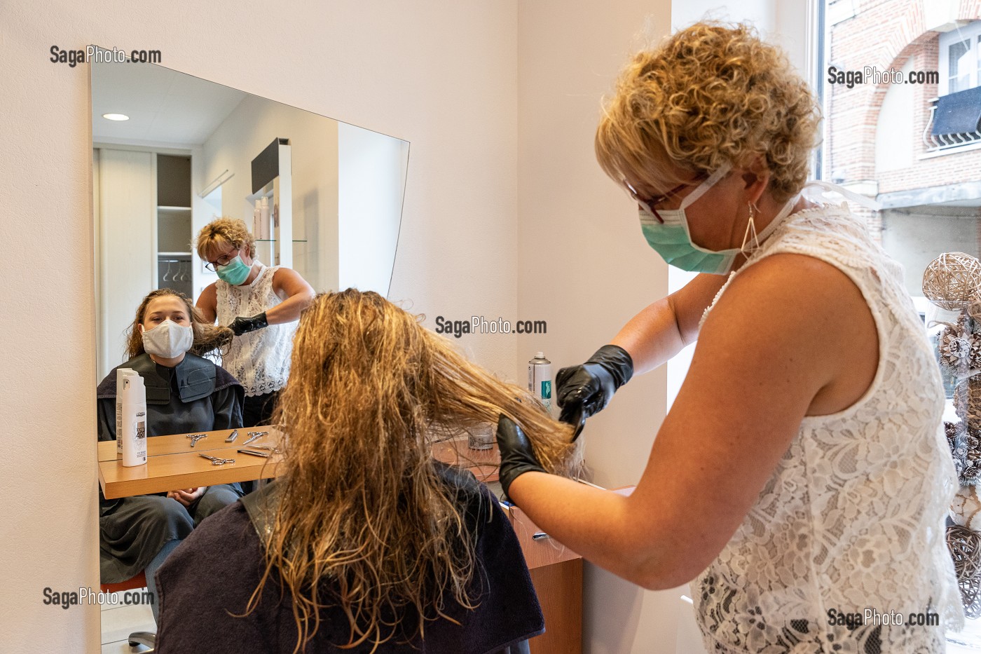 COIFFEUSE AVEC SON MASQUE DE PROTECTION ET SES GANTS EN TRAIN DE COIFFER UNE CLIENTE DANS UN SALON DE COIFFURE VIDE, RUGLES, NORMANDIE, FRANCE 