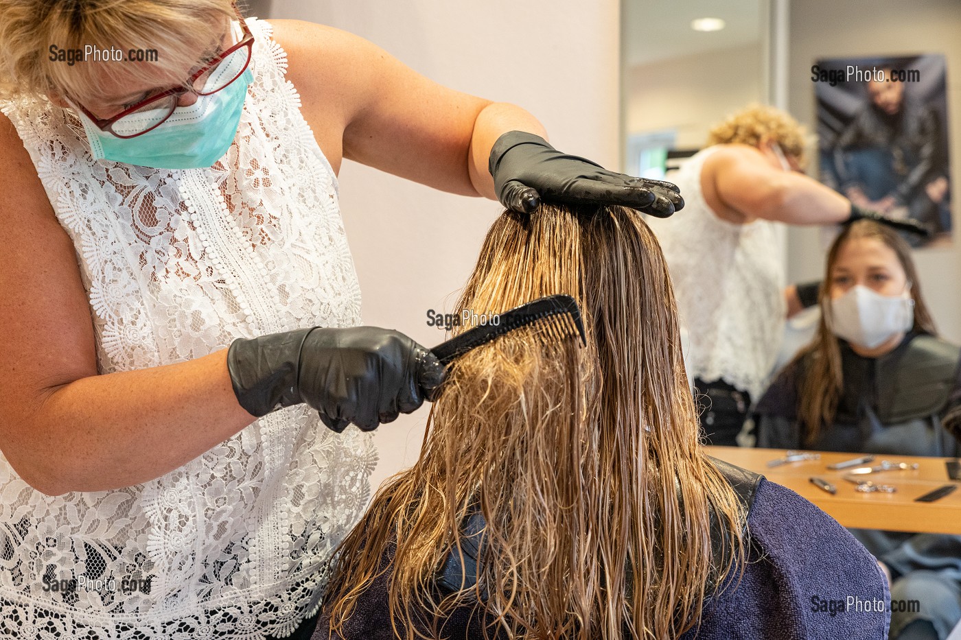 COIFFEUSE AVEC SON MASQUE DE PROTECTION ET SES GANTS EN TRAIN DE COIFFER UNE CLIENTE DANS UN SALON DE COIFFURE VIDE, RUGLES, NORMANDIE, FRANCE 