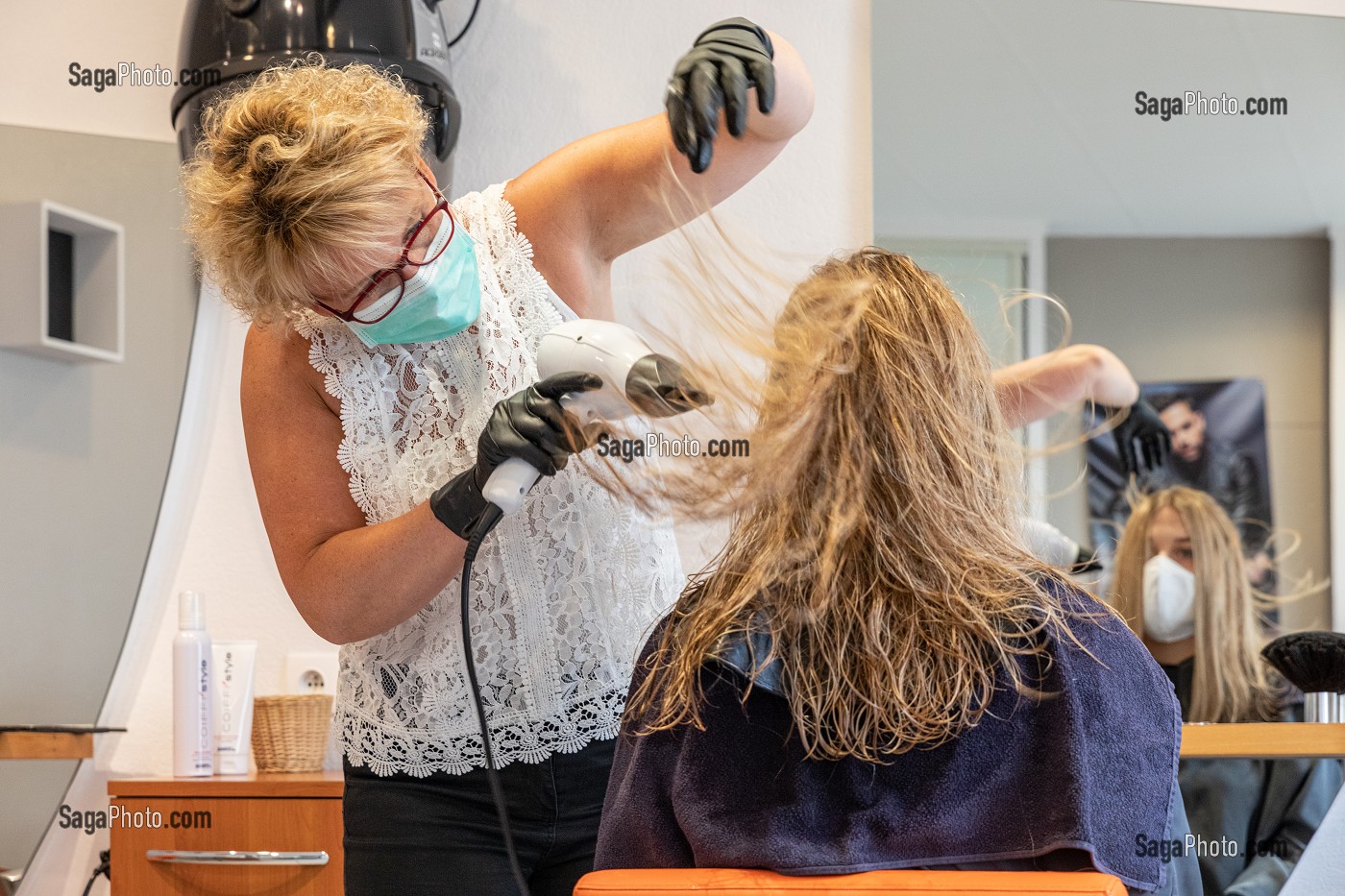 SECHAGE DES CHEVEUX, COIFFEUSE AVEC SON MASQUE DE PROTECTION ET SES GANTS EN TRAIN DE COIFFER UNE CLIENTE DANS LE SALON DE COIFFURE VIDE, RUGLES, NORMANDIE, FRANCE 