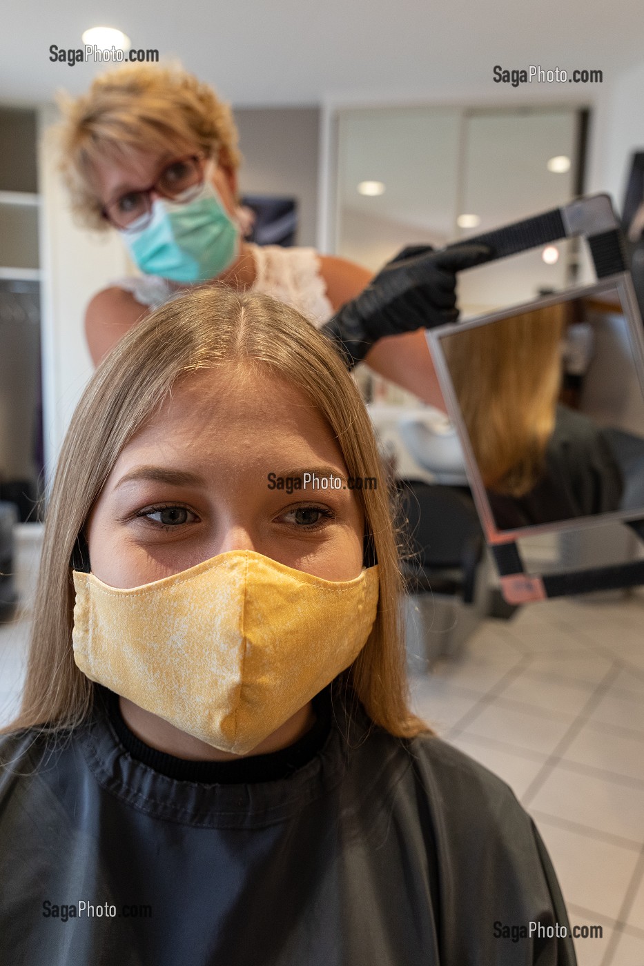 COIFFEUSE AVEC SON MASQUE DE PROTECTION ET SES GANTS EN TRAIN DE COIFFER UNE CLIENTE DANS UN SALON DE COIFFURE VIDE, RUGLES, NORMANDIE, FRANCE 