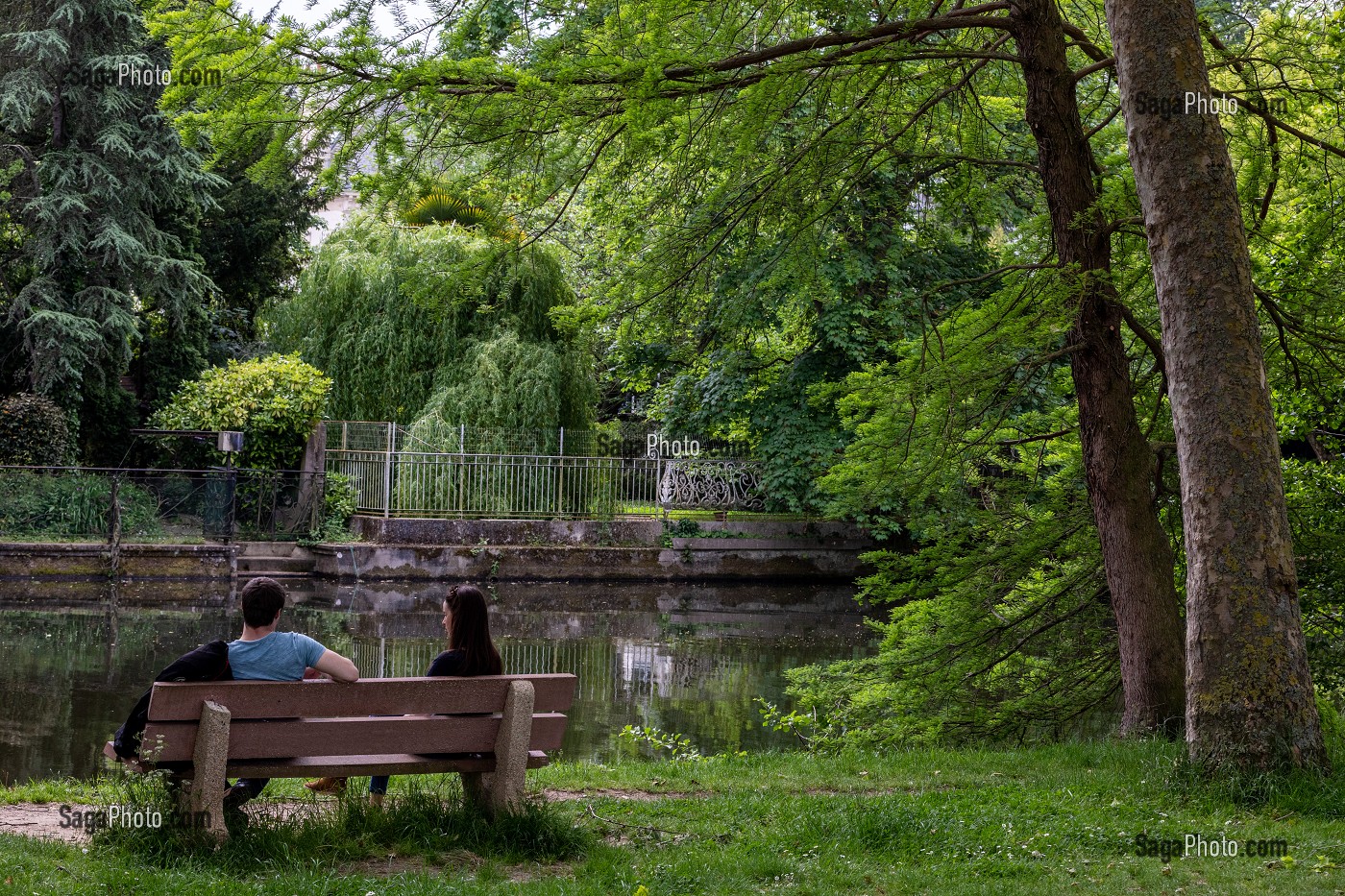 JEUNE COUPLE ASSIS SUR UN BANC SUR LES BORDS DE L'ORNE, LA PRAIRIE, CAEN, CALVADOS, NORMANDIE, FRANCE 