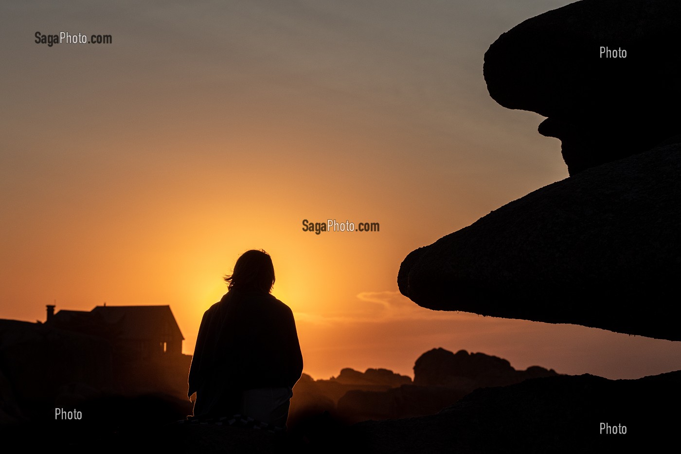 FEMME ASSISE SUR LES ROCHERS AU COUCHER DE SOLEIL, POINTE DE L'ILE RENOTE, TREGASTEL, COTE DE GRANIT ROSE, COTES-D’ARMOR, BRETAGNE, FRANCE 