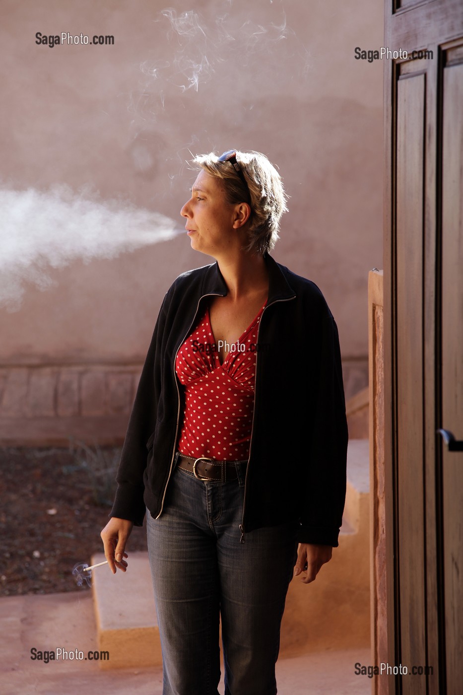 LOI CONTRE LE TABAGISME, FEMME FUMANT DEHORS, SUR LE PAS DE SA PORTE 