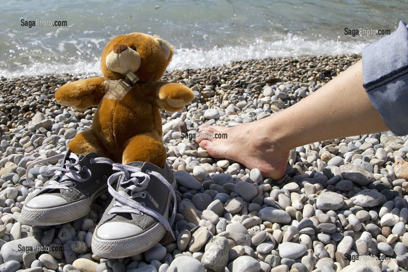 TEDDY L'OURS EN PELUCHE S'AMUSANT SUR UNE PLAGE DE GALETS 