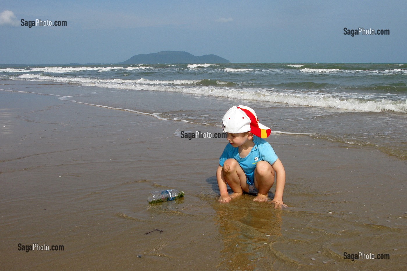 ENFANT SUR LA PLAGE JOUANT AVEC UNE BOUTEILLE EN PLASTIQUE REJETE PAR LA MER 
