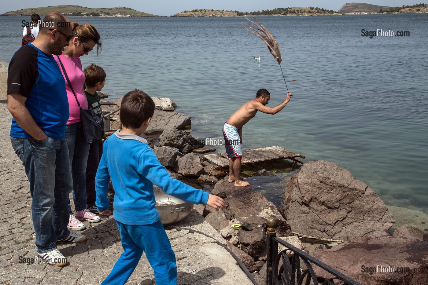 RETOUR DE LA PECHE, TOURISTES DEVANT LE PECHEUR EN TRAIN DE BATTRE DES POULPES, SORTE DE PIEUVRE, PORT DE FOCA SUR LA MER EGEE,  RIVIERA DES OLIVIERS, NORD D’IZMIR, TURQUIE 
