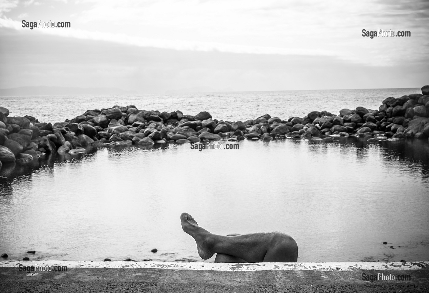 PIED ET JAMBE D'UN TOURISTE DERRIERE UN MURET DEVANT LA MER, CANICO, MADERE, PORTUGAL 