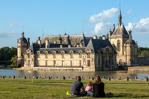 FAMILLE ASSISE SUR LES PELOUSES FACE AU CHATEAU DE CHANTILLY ET A SES DOUVES, OISE (60), FRANCE