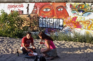 COUPLE AU BORD DE SPREE DEVANT LE MUR DE BERLIN SUR LE SITE DE EAST SIDE GALLERY (MAUER GALERIE), BERLIN, ALLEMAGNE 