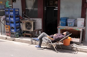 COMMERCANT FAISANT LA SIESTE DEVANT LA DEVANTURE DE SA BOUTIQUE DANS LA VIEILLE VILLE DE SHANGHAI, QUARTIER DE PUXI, SHANGHAI, REPUBLIQUE POPULAIRE DE CHINE 