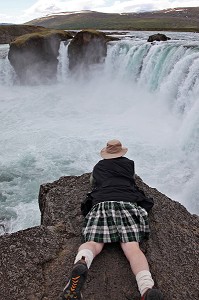 HOMME ALLONGE EN KILT AU BORD DES CHUTES DE GODAFOSS, CASCADE DES DIEUX, NORD DE L'ISLANDE, EUROPE, ISLANDE 