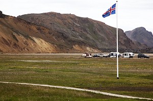 DRAPEAU ISLANDAIS FLOTTANT SUR LE CAMPING DE LANDMANNALAUGAR, AU CENTRE DE L'ISLANDE. PAYSAGE TOURMENTE OU L'ACTIVITE VOLCANIQUE A FORME DES CRATERES ROUGEATRES ET DES MONTAGNES DE RHYOLITE, HAUTES TERRES D’ISLANDE, EUROPE 