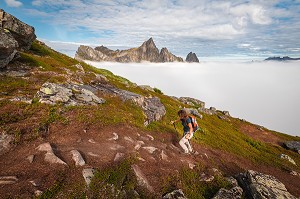 RANDONNEUSE MONTANT LA MONTAGNE HESTEN, PAROIS DU INSTE KONGEN EMERGEANT D'UNE MER DE NUAGES EN ARRIERE-PLAN, FJORDGARD, SENJA, NORVEGE 