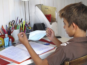 ENFANT FAISANT SES DEVOIRS AVEC UN MASQUE CHIRURGICAL DANS SA CHAMBRE, GESTES DE PREVENTION ET DE LUTTE CONTRE LE VIRUS H1N1 OU LA GRIPPE A 