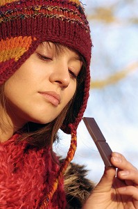 FROID ET CALORIES. JEUNE FEMME MANGEANT DU CHOCOLAT LORS D'UNE PROMENADE EN FORET 