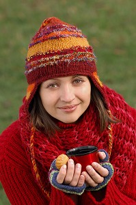 FROID ET CALORIES. JEUNE FEMME SE RECHAUFFANT ET SE RESTAURANT AVEC UNE BOISSON CHAUDE ET UN PETIT GATEAU, LORS D'UNE PROMENADE DANS LA NATURE 