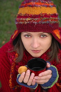 FROID ET CALORIES. JEUNE FEMME SE RECHAUFFANT ET SE RESTAURANT AVEC UNE BOISSON CHAUDE ET UN PETIT GATEAU, LORS D'UNE PROMENADE DANS LA NATURE 