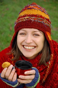 FROID ET CALORIES. JEUNE FEMME SE RECHAUFFANT ET SE RESTAURANT AVEC UNE BOISSON CHAUDE ET UN PETIT GATEAU, LORS D'UNE PROMENADE DANS LA NATURE 