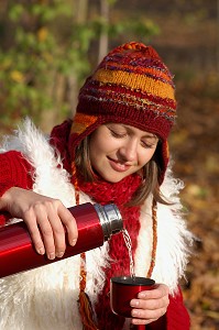 JEUNE FEMME SE SERVANT UNE BOISSON CHAUDE LORS D'UNE PROMENADE DANS LA NATURE 