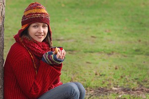 FROID ET CALORIES. JEUNE FEMME SE RECHAUFFANT ET SE RESTAURANT AVEC UNE BOISSON CHAUDE ET UN PETIT GATEAU, LORS D'UNE PROMENADE DANS LA NATURE 