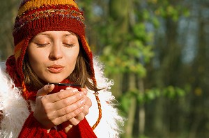 JEUNE FEMME SE RECHAUFFANT AVEC UNE BOISSON CHAUDE, LORS D'UNE PROMENADE EN FORET 