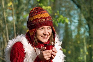 JEUNE FEMME SE RECHAUFFANT AVEC UNE BOISSON CHAUDE, LORS D'UNE PROMENADE EN FORET 