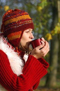 JEUNE FEMME SE RECHAUFFANT AVEC UNE BOISSON CHAUDE, LORS D'UNE PROMENADE EN FORET 