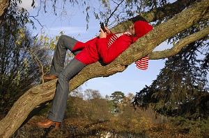 NATURE ET TECHNOLOGIE. JEUNE FEMME ECOUTANT DE LA MUSIQUE AVEC SON TELEPHONE PORTABLE, SUR UNE BRANCHE D'ARBRE, EN FORET 