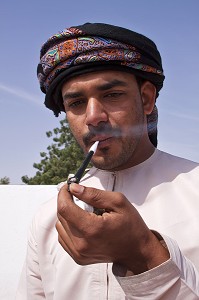 HOMME EN HABIT TRADITIONNEL (DISHDASHA) FUMANT LA PIPE OMANAISE, ROUTE DE WAHIBA SANDS, SULTANAT D'OMAN, MOYEN-ORIENT 